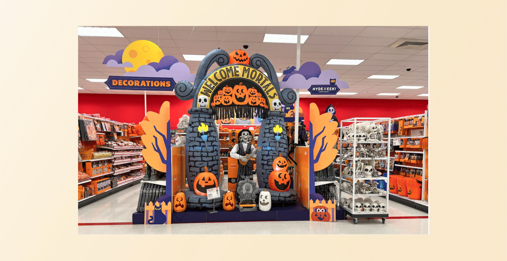 Colorful Halloween store display featuring a carved pumpkin arch, skulls, and a sign reading 'Welcome Mortals' with pumpkins and skeletons in the scene.